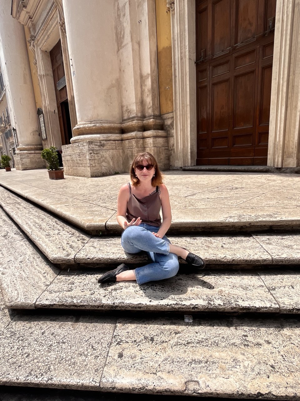 Yana Litinskaya sitting on stone steps outside a classical building in Rome